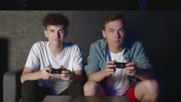 Twee overstuur jongens zitten op de bank voor de TV en verliezen in een spel op de console - Video