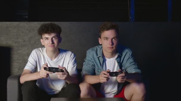 Két fiatal barát akcióvideojátékozik a nappaliban, a kanapén ülve. Egyikük befejezte a játékot, elbúcsúzott és elment. - Felvétel, videó