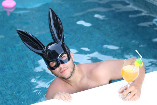 közeli kép jóképű fiatalember latex nyuszi maszk pihentető medence - Fotó, kép