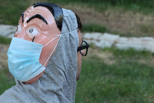 крупним планом портрет красивого молодого чоловіка з пластиковою маскою обличчя на спині та медичною маскою для захисту ковадла в зеленому парку
 - Фото, зображення