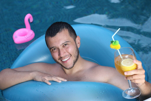 Kokteyl ve yüzme havuzunda gevşeyen şişme tüplü yakışıklı genç adamın yakın plan portresi. - Fotoğraf, Görsel