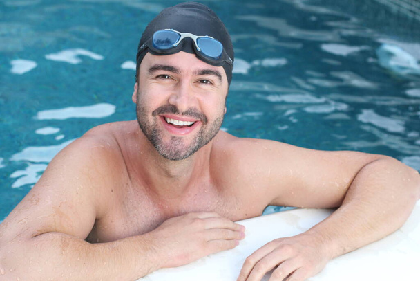 Nahaufnahme Porträt eines gutaussehenden jungen Mannes mit Schwimmbrille und Gummimütze im Schwimmbad - Foto, Bild