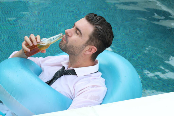 Крупный план портрета красивого молодого человека в белой рубашке с галстуком, держащего бутылку пива во время отдыха в бассейне - Фото, изображение