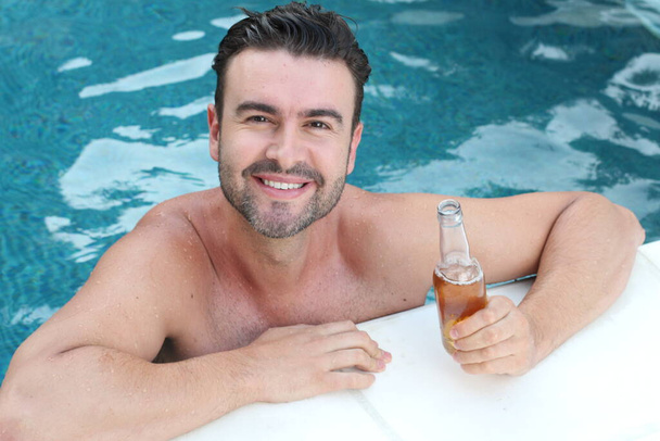 close-up portrait of handsome young man with bottle of beer relaxing in swimming pool - Foto, imagen