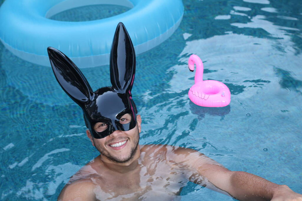 primer plano retrato de joven guapo en látex conejito máscara relajante en la piscina - Foto, Imagen
