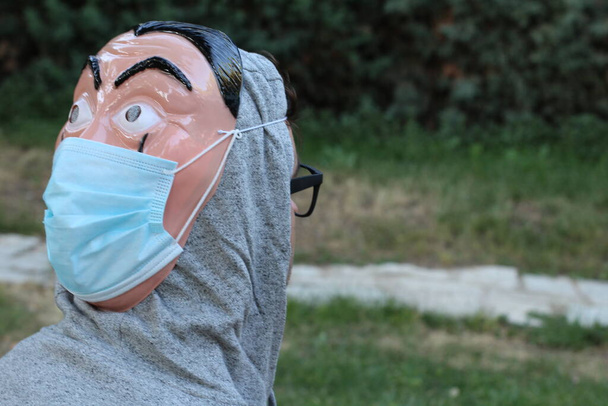 Yeşil Park 'ta korunmak için arka yüzünde plastik maske ve tıbbi maske olan yakışıklı genç adamın yakın plan portresi. - Fotoğraf, Görsel