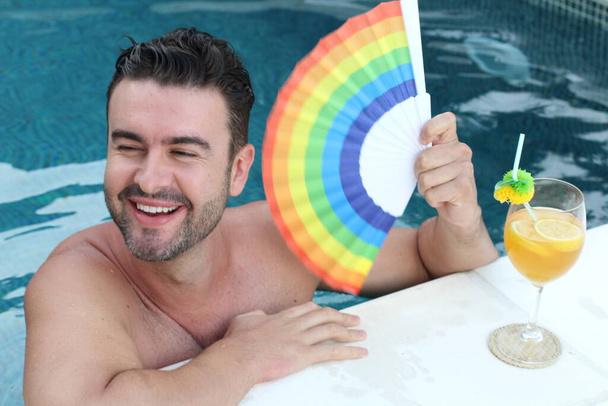 Nahaufnahme Porträt eines hübschen jungen Mannes mit lgbt farbigem Handheld-Ventilator, der sich im Schwimmbad entspannt - Foto, Bild