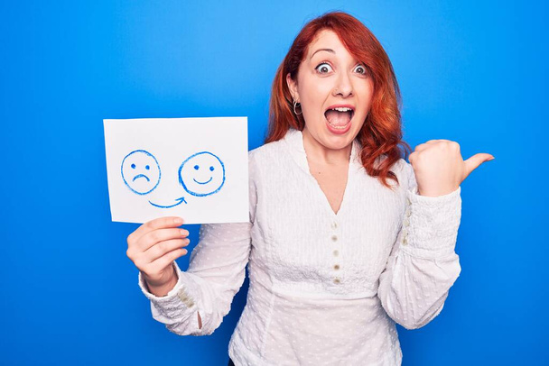 Redhead coach woman asking for depression holding paper with emotion change message pointing thumb up to the side smiling happy with open mouth - Photo, Image