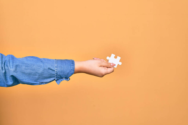 Hand of caucasian young woman holding piece of puzzle over isolated yellow background - Photo, Image