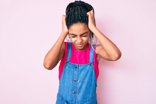 Young african american girl child with braids wearing casual clothes over pink background suffering from headache desperate and stressed because pain and migraine. hands on head.  - Foto, afbeelding