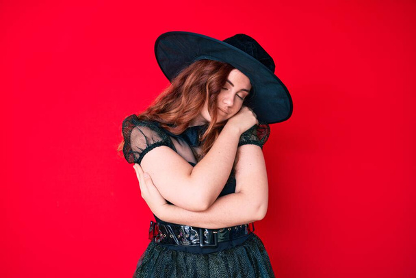Young beautiful woman wearing witch halloween costume hugging oneself happy and positive, smiling confident. self love and self care  - Fotoğraf, Görsel