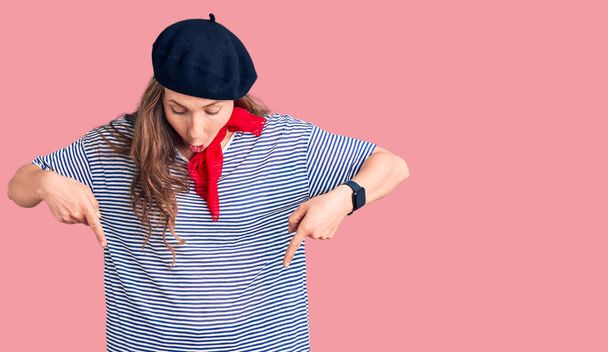 Fiatal gyönyörű szőke nő visel francia svájci sapka és csíkos póló mutató le ujjakkal mutatja a reklám, meglepett arc és nyitott száj  - Fotó, kép