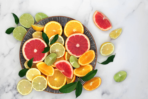 Immuun stimuleren citrusvruchten gezondheid voedsel met sinaasappel, citroen, grapefruit & bladeren op ronde plaat en marmeren achtergrond. Super voedingsmiddelen met een hoog gehalte aan antioxidanten, vitaminen, voedingsvezels en anthocayninen.  - Foto, afbeelding