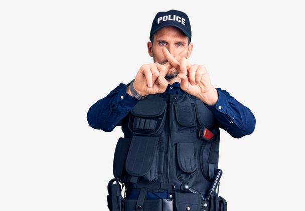 Junger gutaussehender Mann in Polizeiuniform drückt die Daumen und macht ein negatives Zeichen  - Foto, Bild