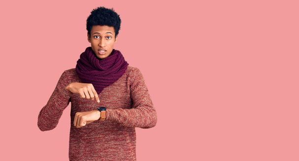 Jonge Afrikaans-Amerikaanse man draagt casual winter trui en sjaal in haast wijzend naar tijd, ongeduld, boos en boos voor deadline vertraging te kijken  - Foto, afbeelding