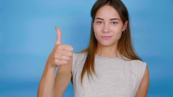 Positieve vrouw in grijs t-shirt heft hand, toont duim omhoog, als en glimlacht - Video