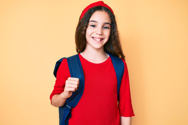 Nettes hispanisches Mädchen mit Studentenrucksack sieht positiv und glücklich stehend aus und lächelt mit einem selbstbewussten Lächeln, das Zähne zeigt  - Foto, Bild