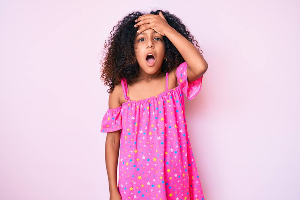 Afrikanisch-amerikanisches Kind mit lockigem Haar in lässigem Kleid überrascht mit der Hand auf dem Kopf für Fehler, erinnere dich an Fehler. Vergessenes, schlechtes Gedächtnis.  - Foto, Bild