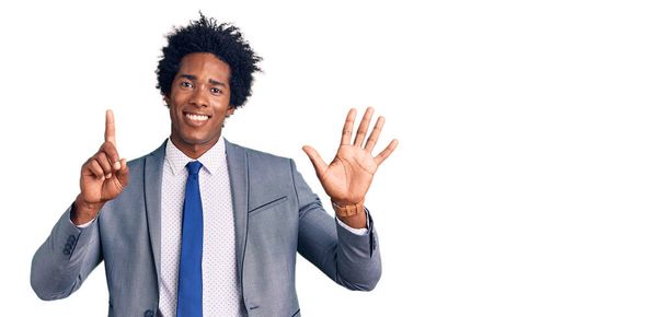 Schöner afrikanisch-amerikanischer Mann mit Afro-Haaren, der Businessjacke trägt und mit Finger Nummer sechs nach oben zeigt, während er selbstbewusst und glücklich lächelt.  - Foto, Bild