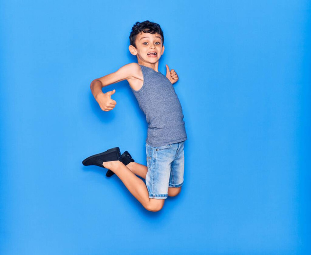 Adorable niño con ropa casual saltando sobre un fondo azul aislado - Foto, Imagen