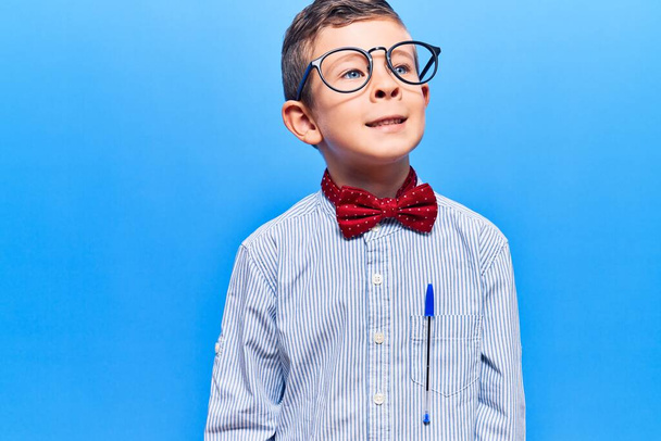 Cute blond kid wearing nerd bow tie and glasses looking away to side with smile on face, natural expression. laughing confident.  - Zdjęcie, obraz