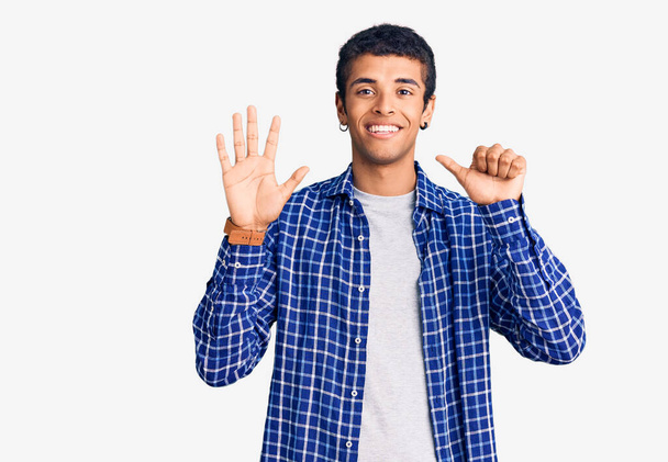 自信と幸せな笑顔ながら、若いアフリカ系アメリカ人の男性は、カジュアルな服を着て指の数6を示すと指摘します.  - 写真・画像