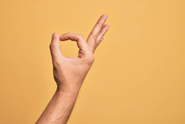 ręka kaukaski młody człowiek pokazujący palce nad odizolowanym żółty tło gestykulujący aprobata wyrażenie robi dobrze symbol z palce - Zdjęcie, obraz