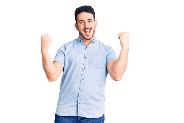 Jovem hispânico vestindo roupas casuais gritando orgulhoso, celebrando vitória e sucesso muito animado com braços levantados  - Foto, Imagem