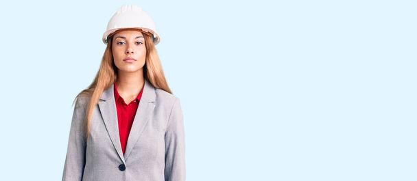 Beautiful young woman wearing architect hardhat relaxed with serious expression on face. simple and natural looking at the camera.  - Photo, Image