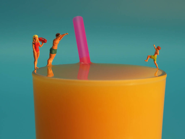Glas Orangensaft mit Strohhalm und drei Miniaturfiguren - Φωτογραφία, εικόνα