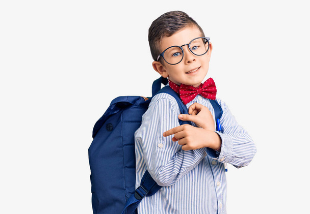 Cute blond kid wearing nerd bow tie and backpack smiling happy pointing with hand and finger  - Fotó, kép