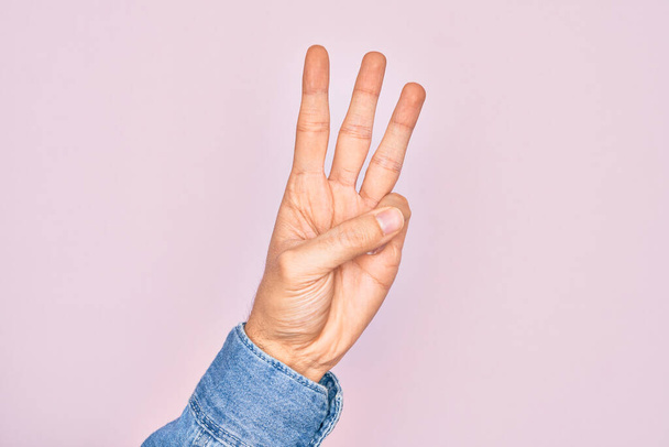 Рука кавказького молодого чоловіка, що показує пальці над ізольованим рожевим тлом, підраховуючи номер 3 з трьома пальцями
 - Фото, зображення
