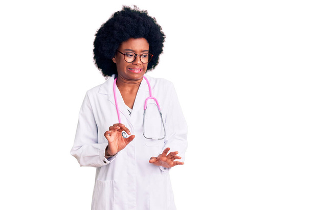Mladá africká Američanka v lékařském kabátě a stetoskopu znechucený výraz, nespokojenost a strach dělá znechucený obličej, protože averzní reakce.  - Fotografie, Obrázek