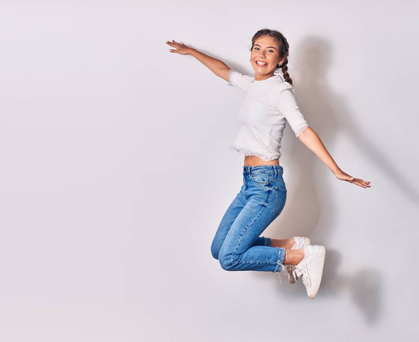 Young beautiful woman with braids wearing casual clothes smiling happy. Jumping with smile on face and arms opened over isolated white background - Fotoğraf, Görsel