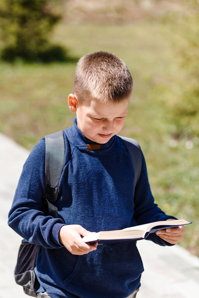 vertical portrait of a schoolboy reading a book outdoors - Фото, зображення