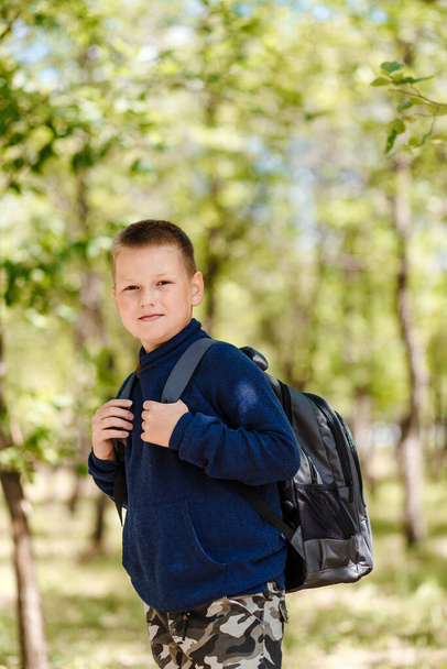 Smiling boy in school uniform with a backpack on his back outdoors - Фото, изображение