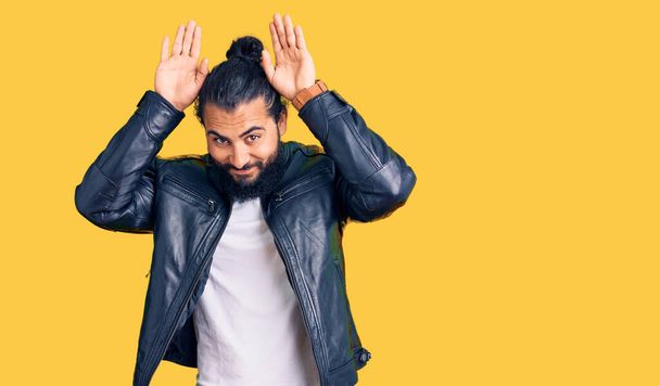 Young arab man wearing casual leather jacket doing bunny ears gesture with hands palms looking cynical and skeptical. easter rabbit concept.  - Photo, Image
