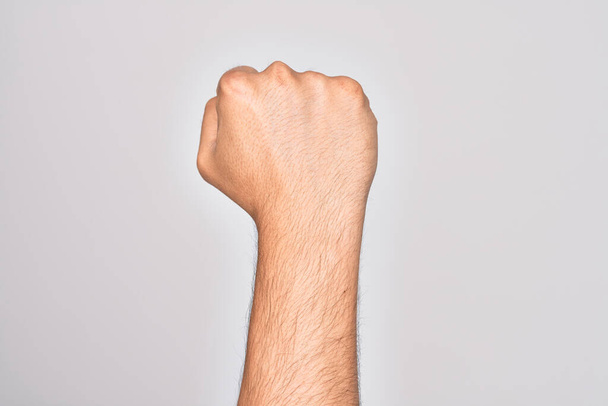 Hand van Kaukasische jongeman met vingers over geïsoleerde witte achtergrond die protesteert en revolutiegebaar maakt, vuist die kracht en macht uitdrukt - Foto, afbeelding