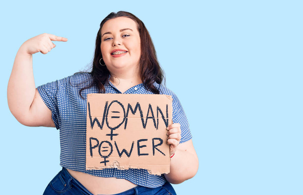 Fiatal plusz méretű nő kezében nő hatalom transzparens mutató ujjal egy önmosolygó boldog és büszke  - Fotó, kép