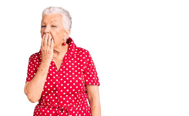 Senior όμορφη γυναίκα με μπλε μάτια και γκρίζα μαλλιά φορώντας ένα κόκκινο καλοκαιρινό φόρεμα βαρεθεί χασμουρητό κουρασμένος καλύπτει το στόμα με το χέρι. ανησυχία και υπνηλία.  - Φωτογραφία, εικόνα