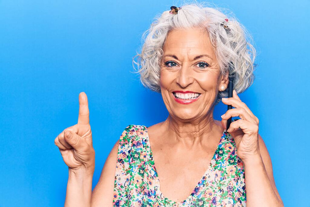 Starsza siwowłosa kobieta rozmawiająca na smartfonie uśmiechnięta pomysłem lub pytaniem wskazującym palcem szczęśliwą twarz, numer jeden  - Zdjęcie, obraz