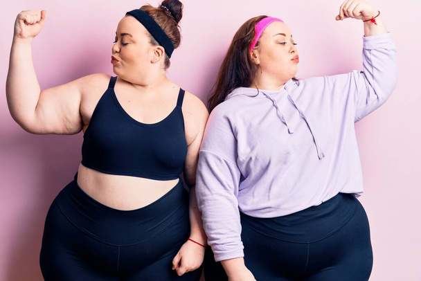Young plus size twins wearing sportswear showing arms muscles smiling proud. fitness concept.  - Фото, изображение