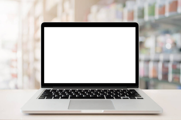 Столешница аптечного магазина с чистым экраном ноутбука над лекарствами на полках в аптеке - Фото, изображение