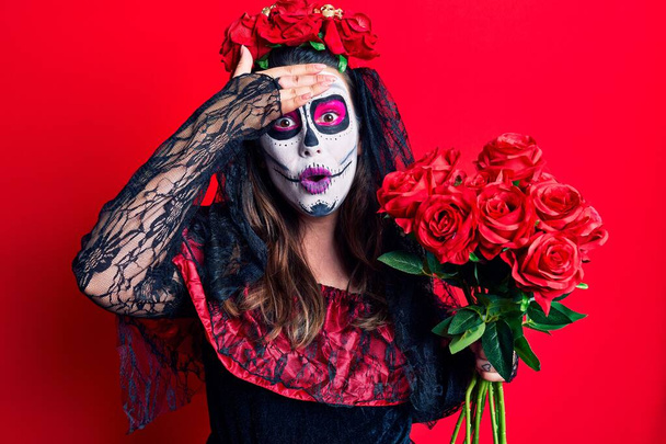 Jovem mulher vestindo dia do traje morto segurando flores estressado e frustrado com a mão na cabeça, rosto surpreso e irritado
  - Foto, Imagem