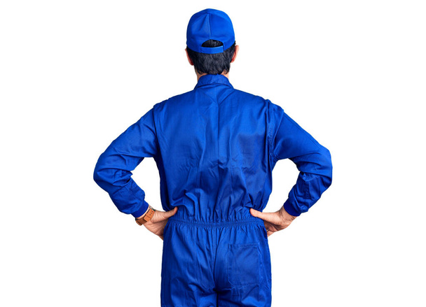 Middle age handsome man wearing mechanic uniform standing backwards looking away with arms on body  - Photo, image