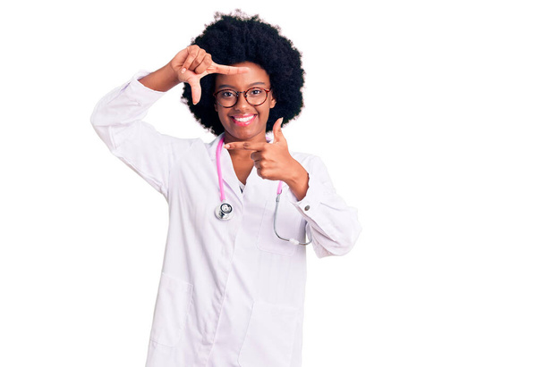 A fiatal afro-amerikai nő orvosi kabátot és sztetoszkópot visel, mosolyog, és keretet csinál kezekkel és ujjakkal, boldog arccal. kreativitás és fényképezés koncepció.  - Fotó, kép