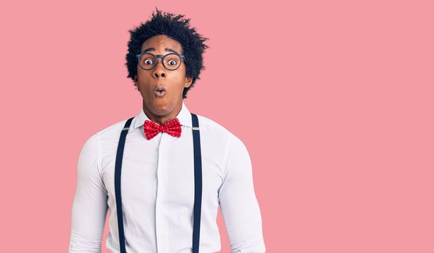Knappe Afro-Amerikaanse man met afro haar draagt hipster elegante blik bang en verbaasd met open mond voor verrassing, ongeloof gezicht  - Foto, afbeelding