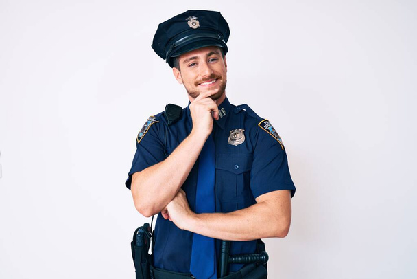 Fiatal fehér férfi rendőregyenruhában, magabiztosan néz a kamerába, keresztbe tett karokkal és felemelt kézzel mosolyog az állára. pozitív gondolkodás.  - Fotó, kép