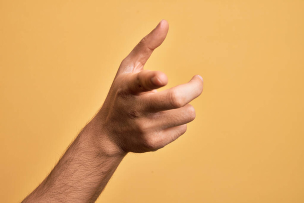 Рука кавказского юноши показывает пальцы на изолированном желтом фоне указывая указательным пальцем на камеру, выбирая и указывая направление - Фото, изображение