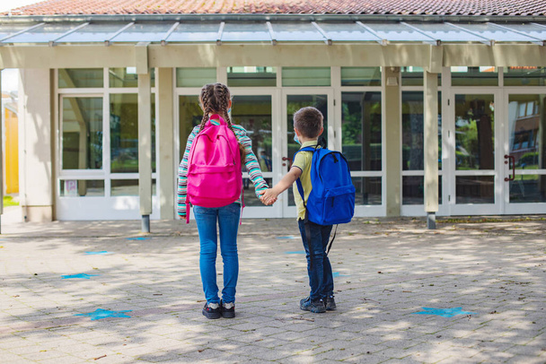 Kız ve erkek kardeşler tatilden sonra okula dönerler. Çocuklar okul kapısının önünde el ele tutuşuyorlar. Yeni okul yılı. - Fotoğraf, Görsel